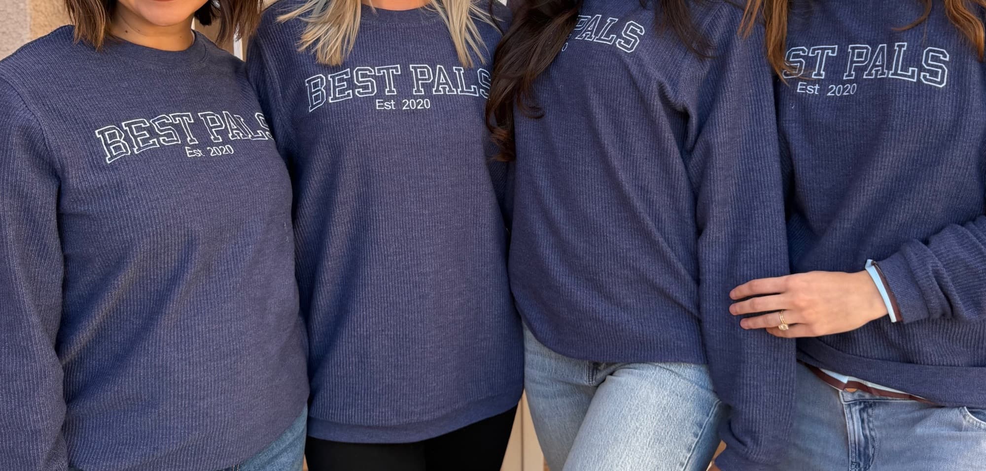 Four friends wearing matching navy corded crewneck sweatshirts embroidered with Best Pals Est 2020