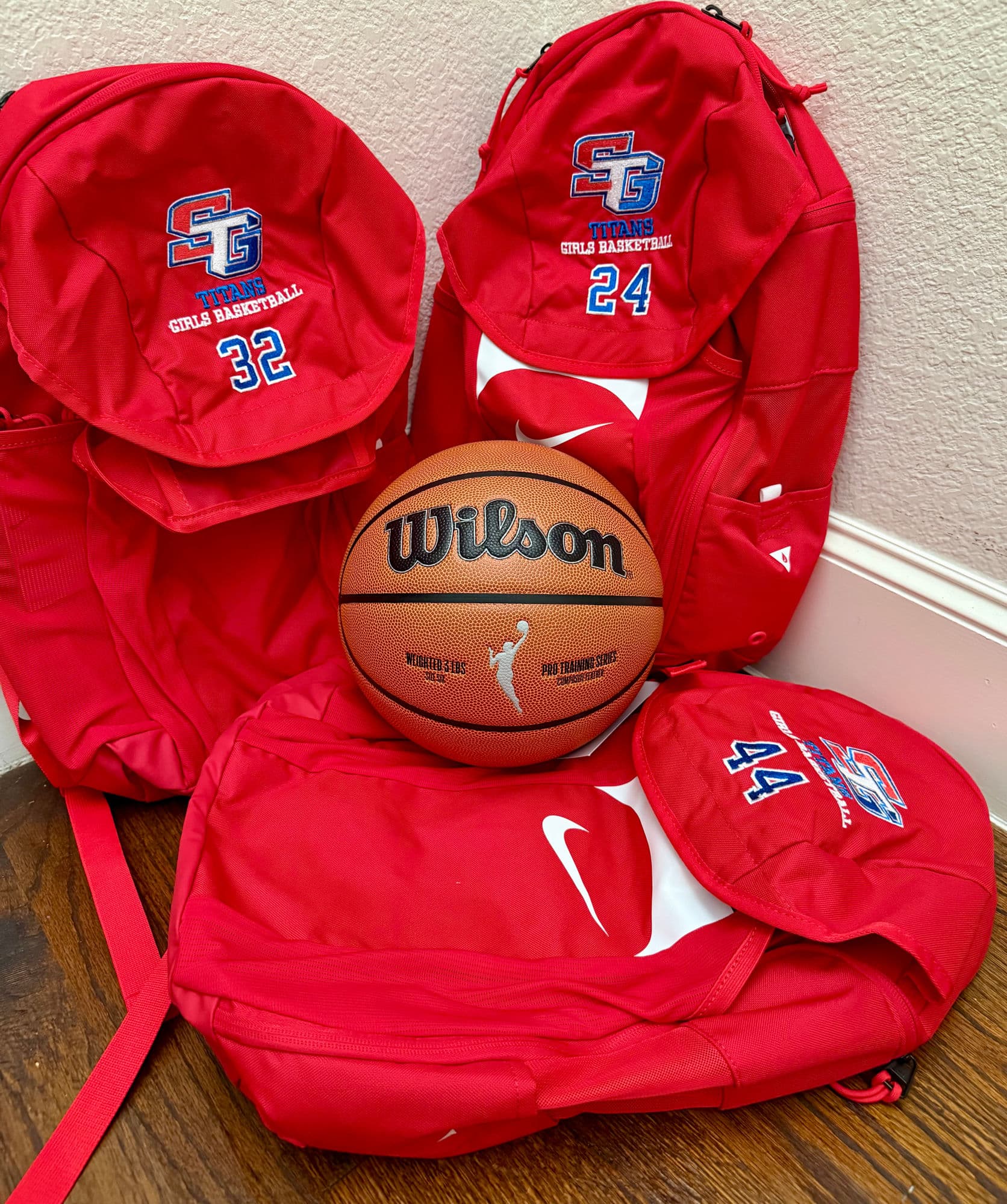 Red Nike backpacks embroidered with the SG Titans girls basketball logo and player numbers